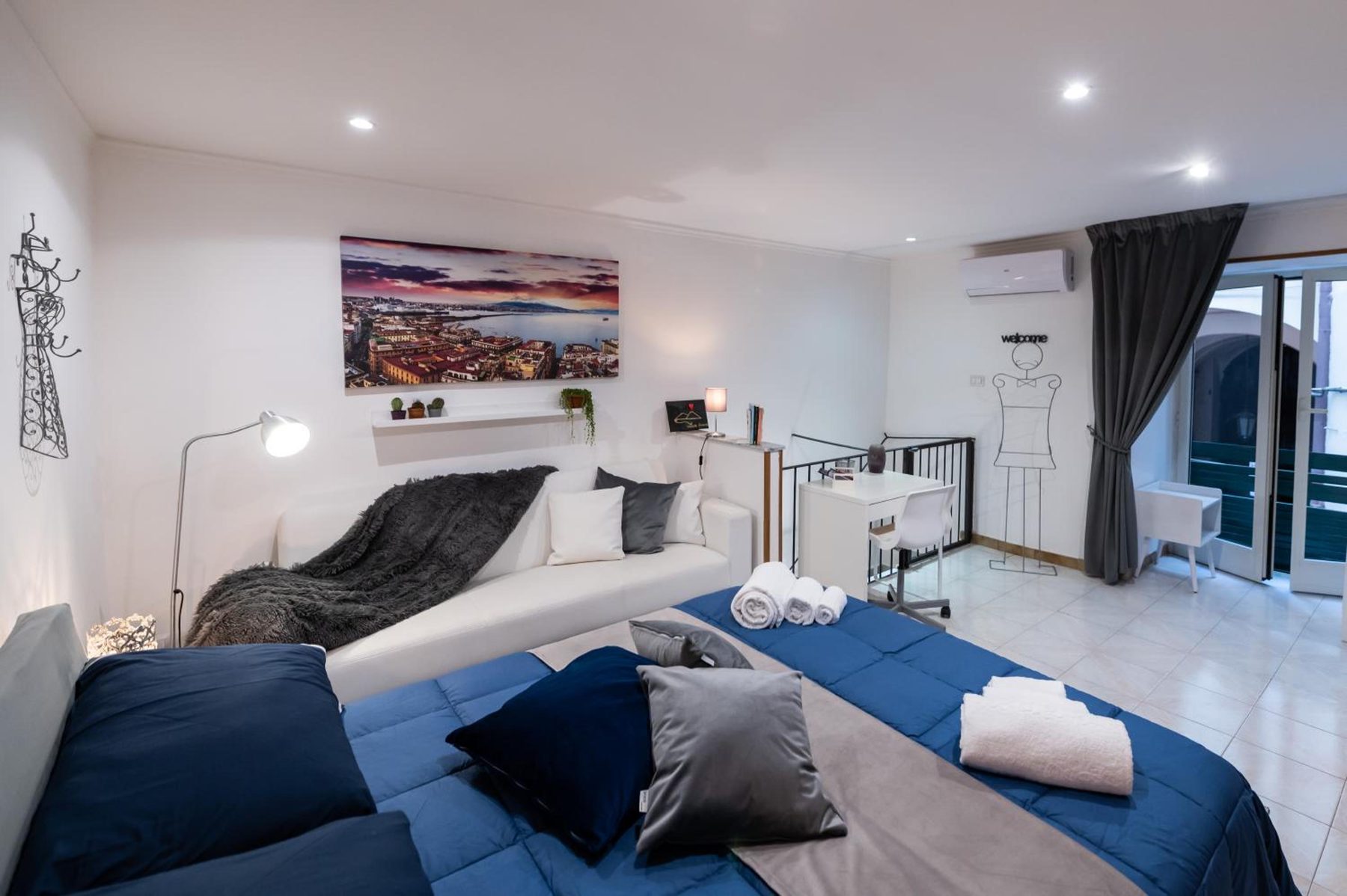 Camera con copriletto blu, cuscini grigi e una stampa del golfo di Napoli sopra il letto