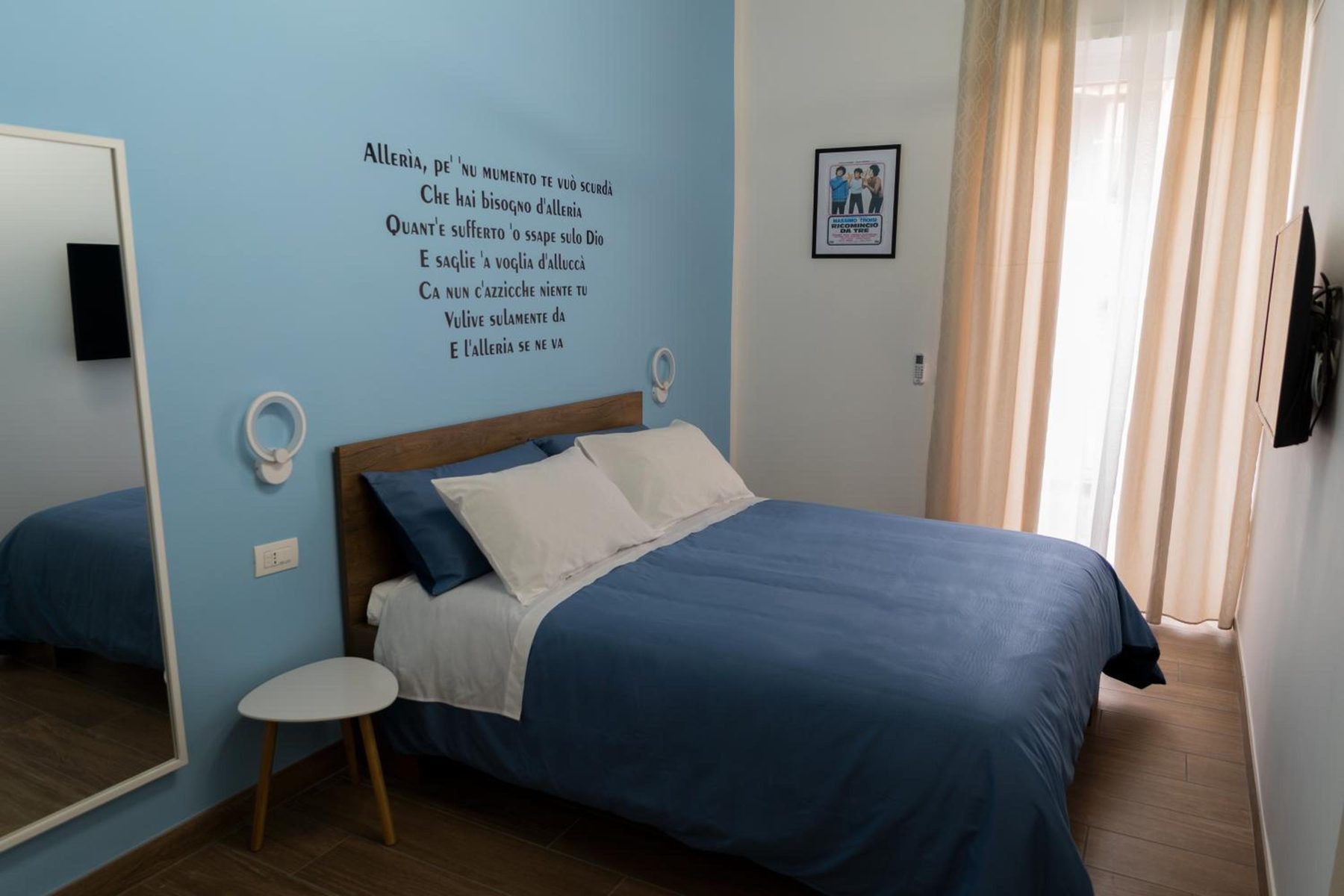 Alleria: letto matrimoniale blu, parete azzurra e la luce della finestra