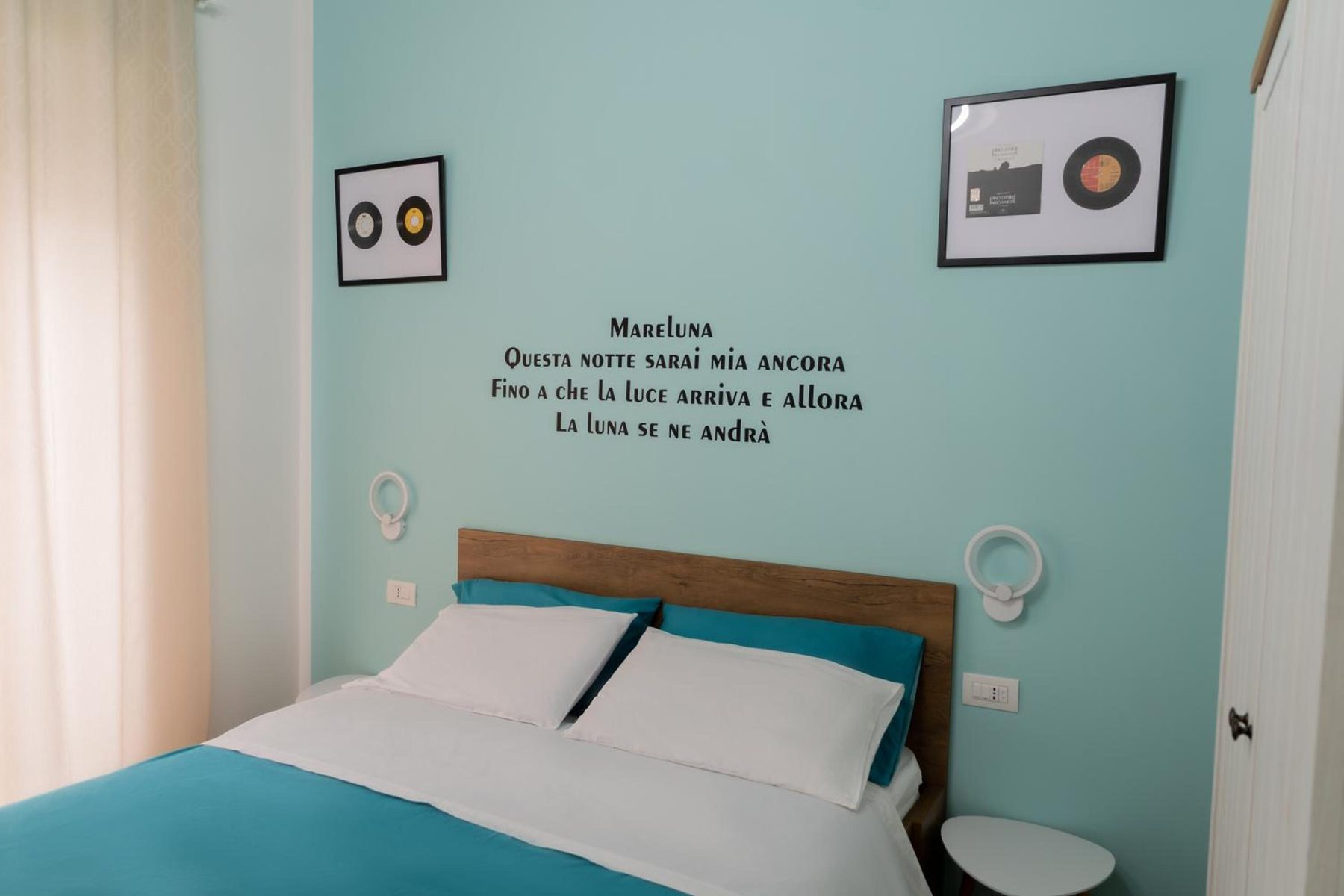 Mareluna: letto con copriletto ottanio, due dischi incorniciati e la parete scritta